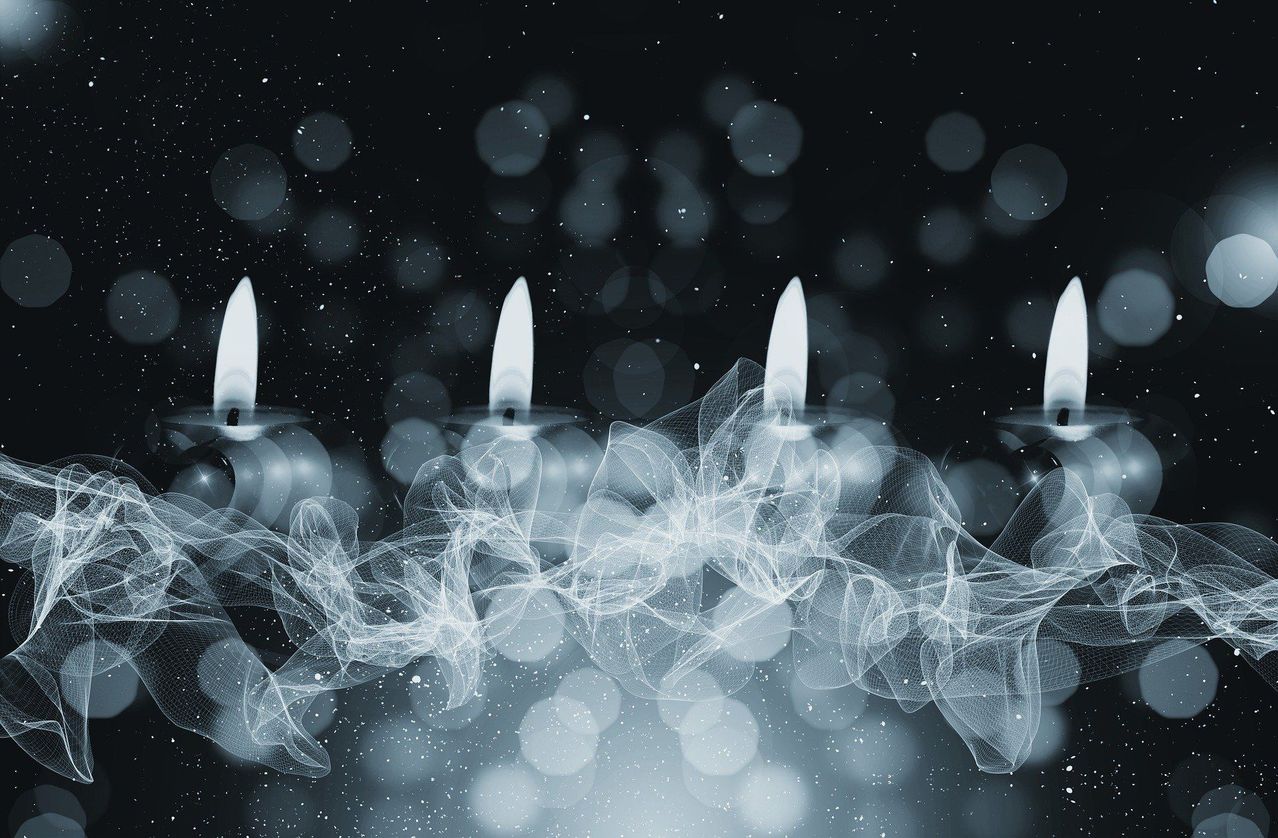 Auf einem schwarzen Hintergrund sind drei brennende Kerzen in einer Reihe zu sehen, aus denen Rauch aufsteigt. Der Hintergrund ist dunkel mit verschwommenen Lichtern.