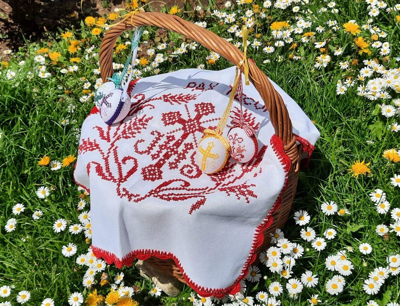 Ein Korb aus Weide mit bestickten Eiern auf einem Feld von Gänseblümchen. Die Eier sind mit Kreuzen und Blumenmustern verziert.