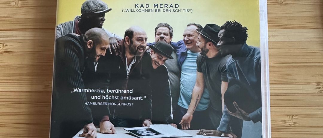 Ein DVD-Cover für den Film 'Ein Triumph' von Emmanuel Courcol, das eine Gruppe von Männern um einen Tisch zeigt, mit einem Zitat und Auszeichnungen auf dem Cover.