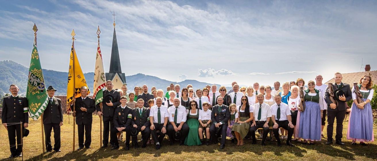 Eine Gruppe von Menschen in traditioneller Kleidung posiert für ein Foto vor einer Kirche mit Bergen im Hintergrund.