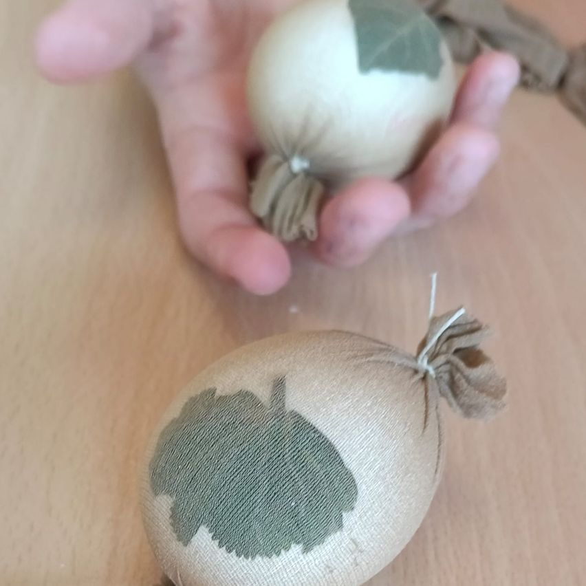 Zwei Eier sind auf einem Holztisch ausgestellt. Eines ist mit einem Blatt verziert und hat eine braune Schleife, während das andere eine braune Schnur hat.