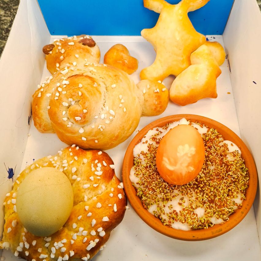 Eine Schachtel mit verschiedenen Gebäckstücken, darunter ein geflochtener Brotkranz mit einem Ei obenauf und eine Schüssel mit einem dekorierten Ei in der Mitte.