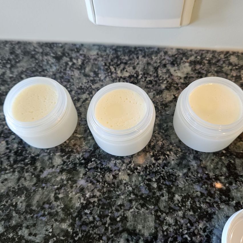 Drei durchsichtige Plastiktöpfe mit Deckeln auf einem Marmortisch. Jeder Topf enthält eine weiße Substanz.