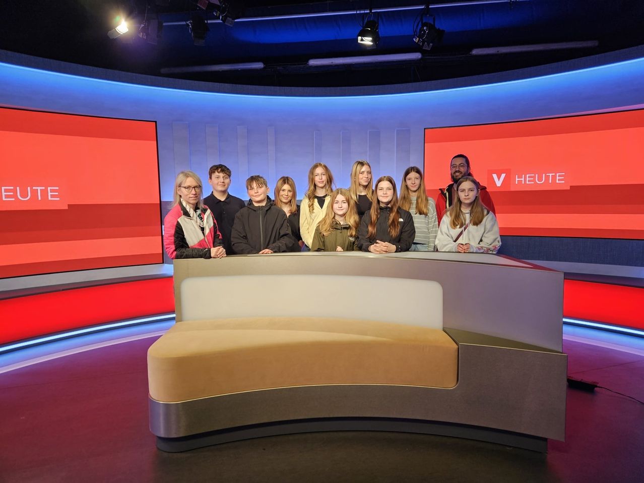 A group of young people and adults are posing for a photo in a studio with red and blue walls and a logo.