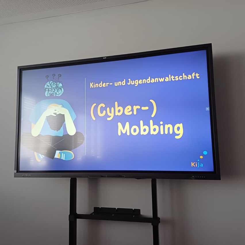 A monitor displays a blue screen with a cartoon person, text 'Kinder- und Jugendanwaltschaft (Cyber-) Mobbing', and logo 'Kija'.