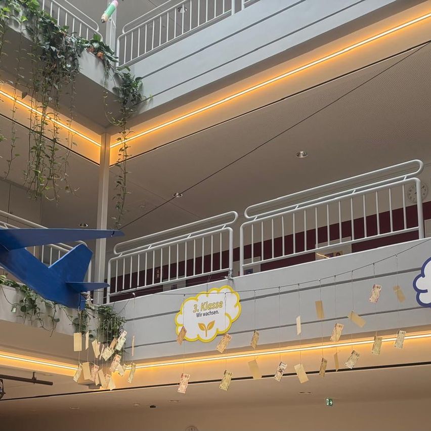 A mall interior with a blue airplane model hanging from the ceiling, a yellow sign with white text, and decorative paper money hanging from the ceiling.