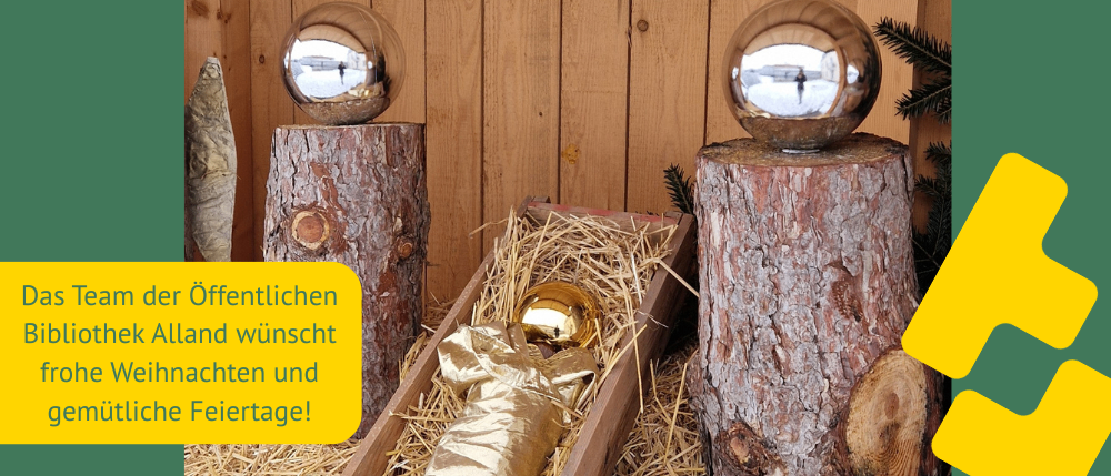 Eine goldene Statue liegt in einer mit Heu gefüllten Holzkiste. Zwei reflektierende Kugeln stehen auf Holzstümpfen. Der Hintergrund ist eine Holzwand mit einem gelben Pfeil, der nach rechts zeigt.