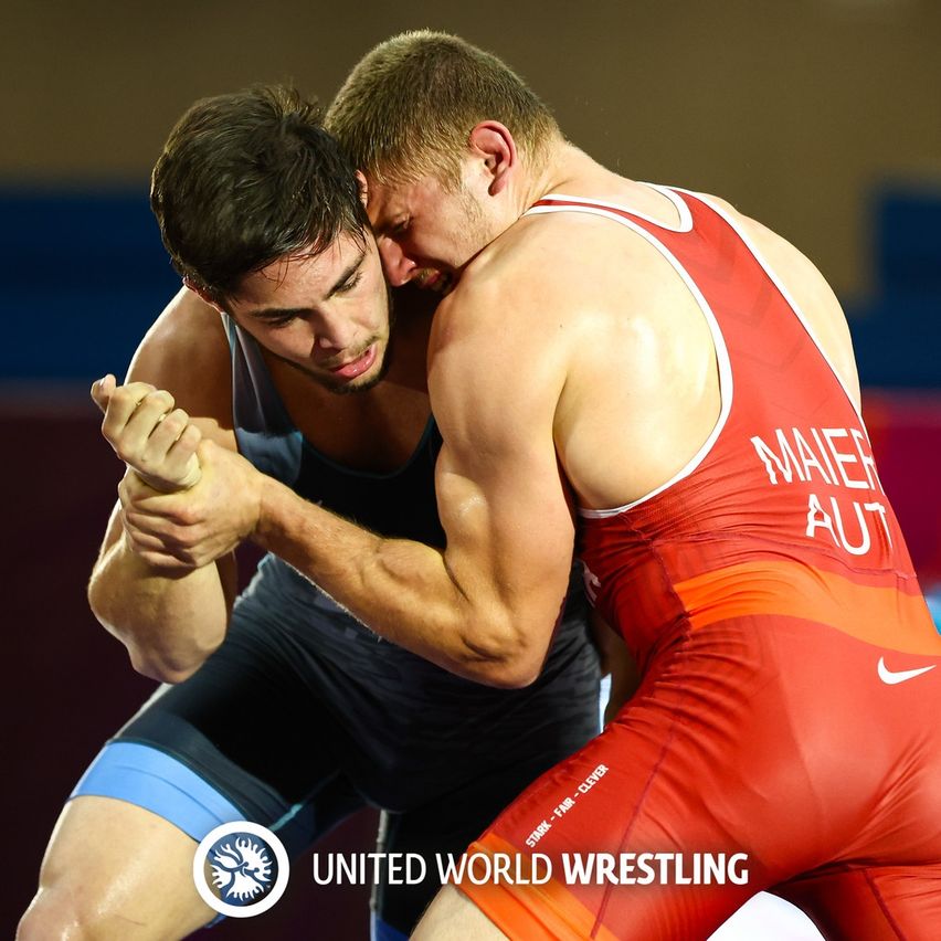 Zwei Ringer kämpfen in einem Ringkampf. Einer trägt ein rotes und weißes Singlet, der andere ist in einem schwarzen Singlet.