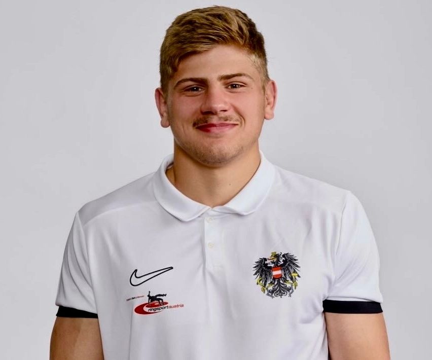 A man wearing a white polo shirt with a Nike logo and a black eagle emblem on the left chest, smiling for a photo.