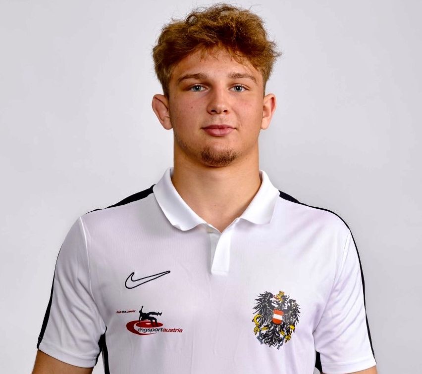 A young man with red hair and a beard wearing a white Nike polo shirt with a black collar and black trims. The shirt features a logo on the left chest and a logo on the right side.