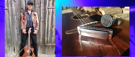 A musician stands with a guitar, a harmonica, and a microphone on a wooden guitar. The background is purple with a wooden fence and a tree trunk.