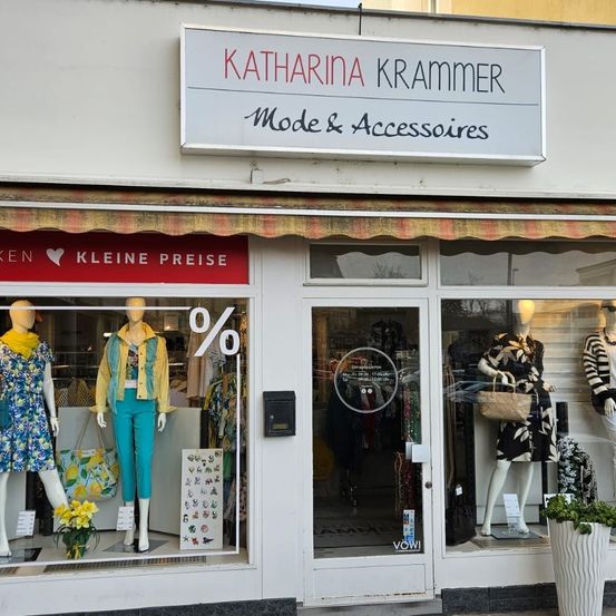 Ein Bekleidungsgeschäft namens Katharina Krammer mit einem Schild, auf dem Mode & Accessoires steht. Mannequins in sommerlicher Kleidung sind im Schaufenster ausgestellt. Der Laden hat ein Ausverkaufsschild mit 0%.