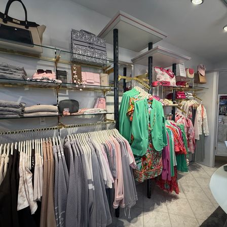 Ein Bekleidungsgeschäft mit Kleiderstangen für verschiedene Kleidungsstücke, von Kleidern bis Hosen, ist gut organisiert mit Regalen, die Handtaschen und Accessoires präsentieren.