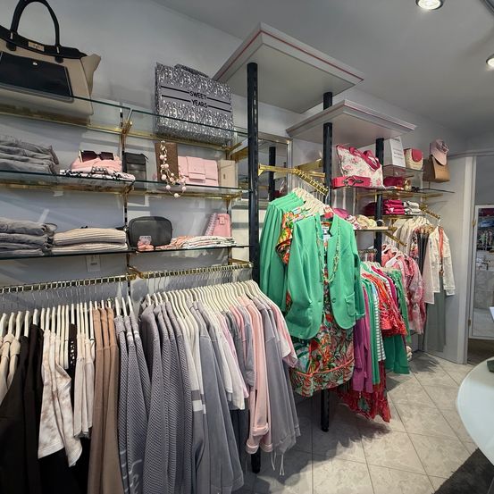 Ein Bekleidungsgeschäft mit Kleiderstangen für verschiedene Kleidungsstücke, von Kleidern bis Hosen, ist gut organisiert mit Regalen, die Handtaschen und Accessoires präsentieren.