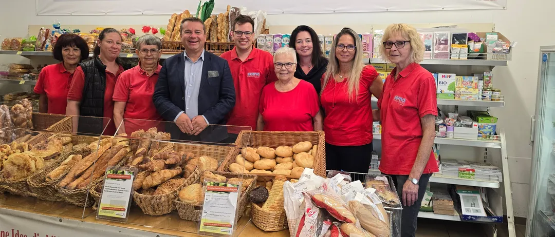 Eine Gruppe von Menschen in roten Hemden steht hinter einer Bäckereitheke mit verschiedenen Broten und Gebäck zur Schau. Darüber befinden sich Gemälde von Früchten.