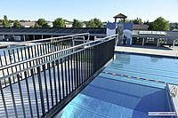 Ein großer Außenpool mit einer Metallbrüstung und einem Turm in der Ferne. Im Hintergrund sind Bäume und Gebäude zu sehen.