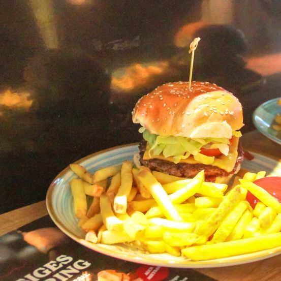Ein Burger mit Salat, Tomate und Käse auf einem Teller mit Pommes Frites, überzogen mit Ketchup.