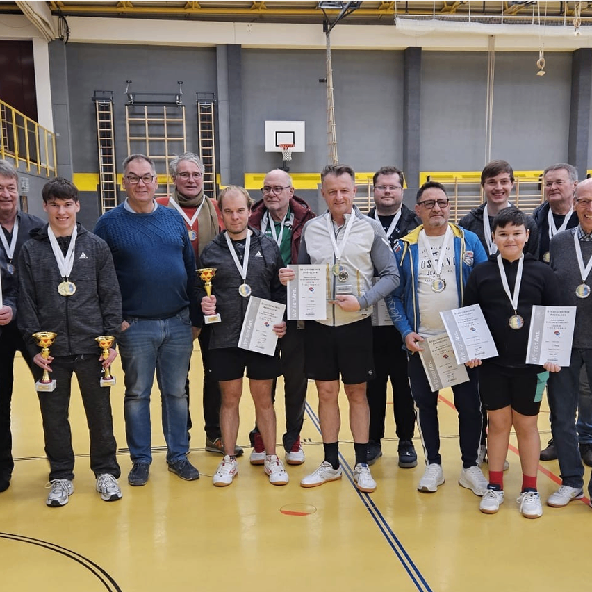 Gruppe von Männern, möglicherweise Athleten, mit Medaillen und Zertifikaten und Pokalen, die auf einem Spielfeld stehen. Einige tragen Brillen und Turnschuhe. Das Spielfeld hat Markierungen und einen Basketballkorb.