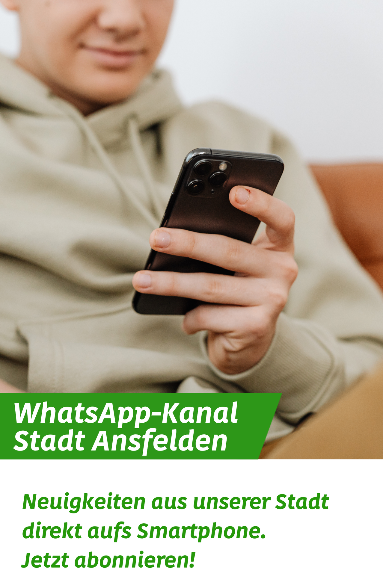 Eine Person in einer beigen Kapuzenjacke hält ein schwarzes Smartphone mit einem grünen Banner darunter, das 'WhatsApp-Kanal Stadt Ansfelden' besagt.