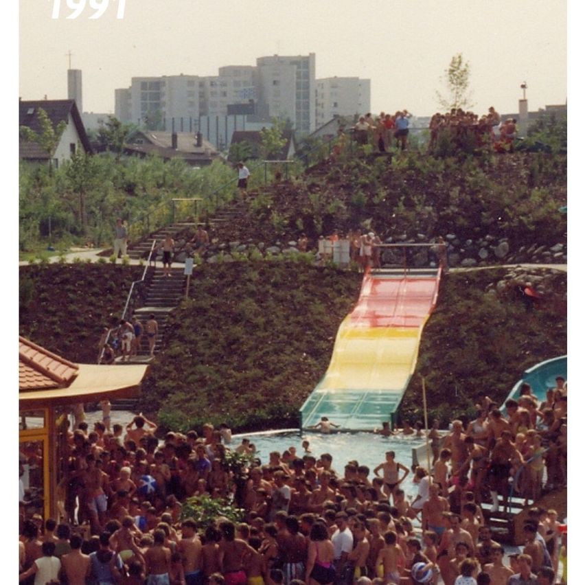 A crowd of people in a pool, some near a slide. The image is dated 1991.