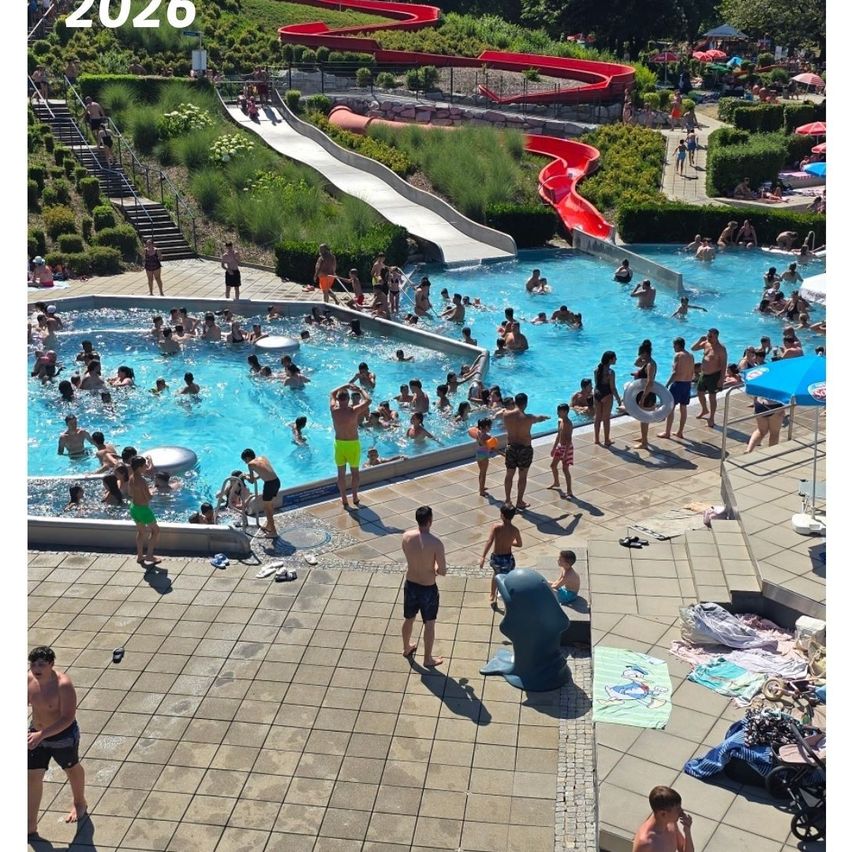 A large group of people are enjoying the swimming pool and slides at an outdoor water park. Some are swimming while others relax on the pool deck.