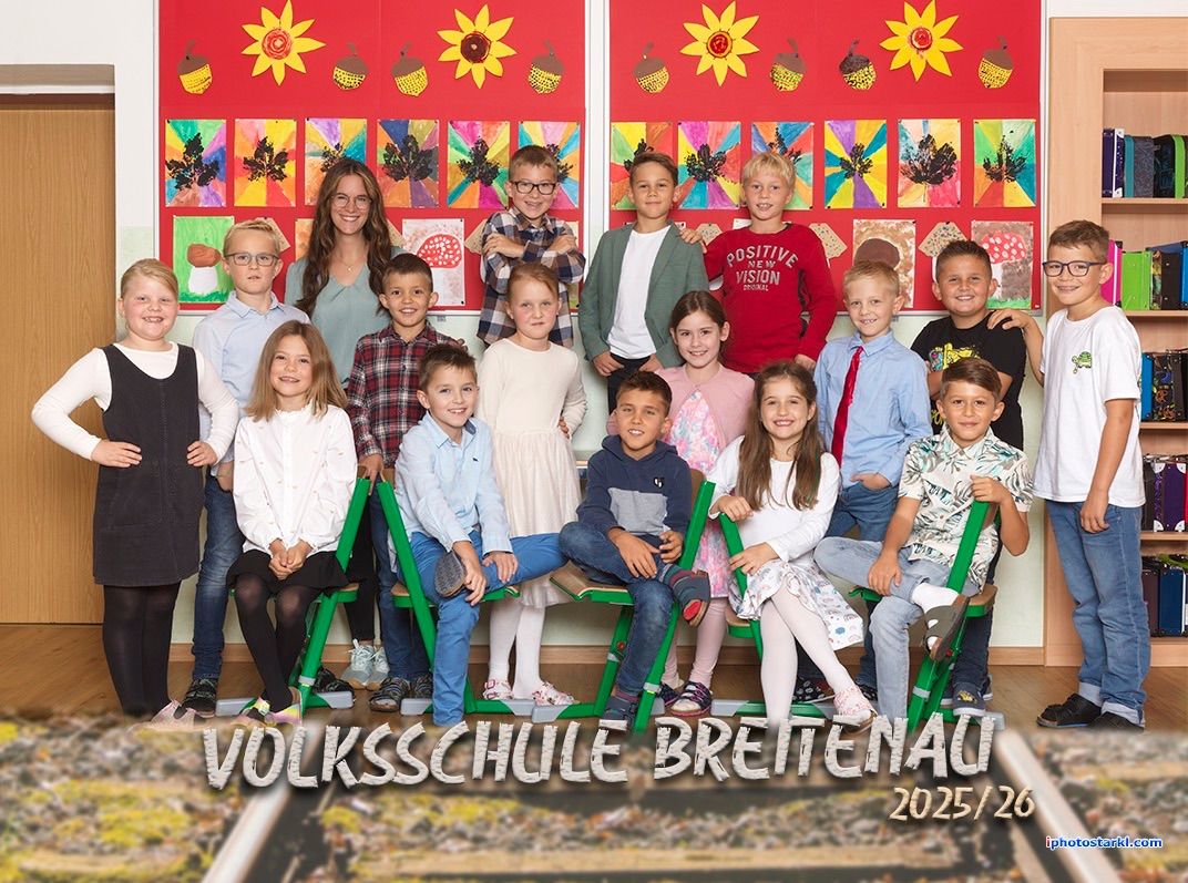 Eine Gruppe von Schülern und ihrer Lehrerin posiert für ein Foto vor einer mit Herbstblättern und Sonnenblumen dekorierten Wand. Der Text 'Volksschule Brettenau 2025/26' ist unten angezeigt.