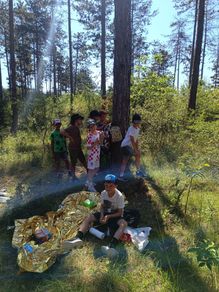 Eine Gruppe von Kindern steht und sitzt in einem Wald, einer mit einem Rucksack und einem anderen mit einem Gips auf dem Bein.