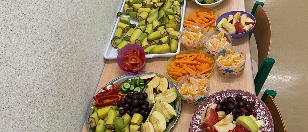 Ein Tisch mit mehreren Platten verschiedener Obst- und Gemüsesorten, einschließlich Äpfel, Karotten und Bananen, in Buffet-Stil angeordnet.