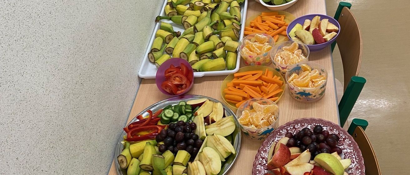 Ein Tisch mit mehreren Platten verschiedener Obst- und Gemüsesorten, einschließlich Äpfel, Karotten und Bananen, in Buffet-Stil angeordnet.