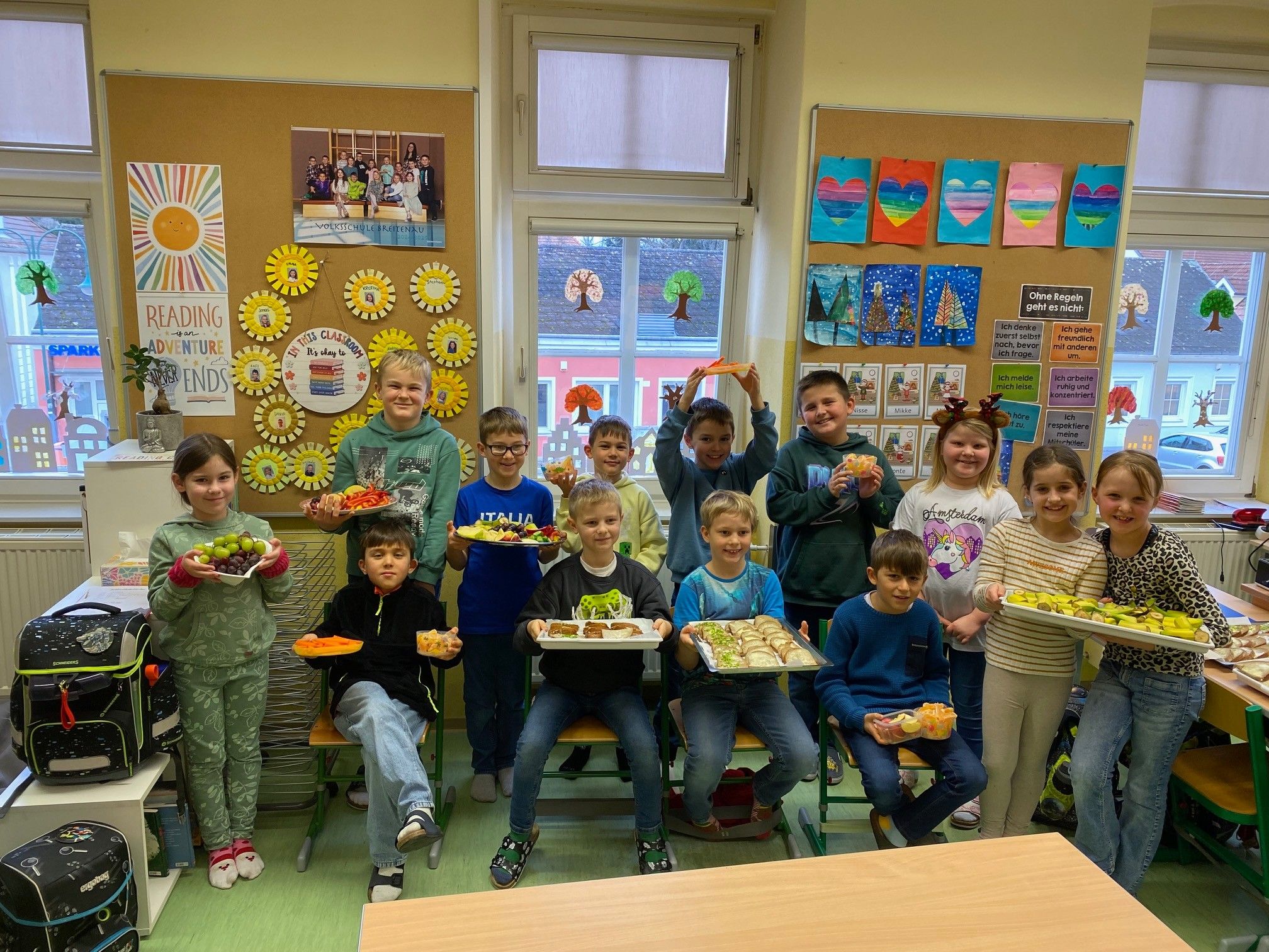 Eine Gruppe von Kindern in einem Klassenzimmer hält Tabletts mit Essen darauf. Sie lächeln und posieren für ein Foto.