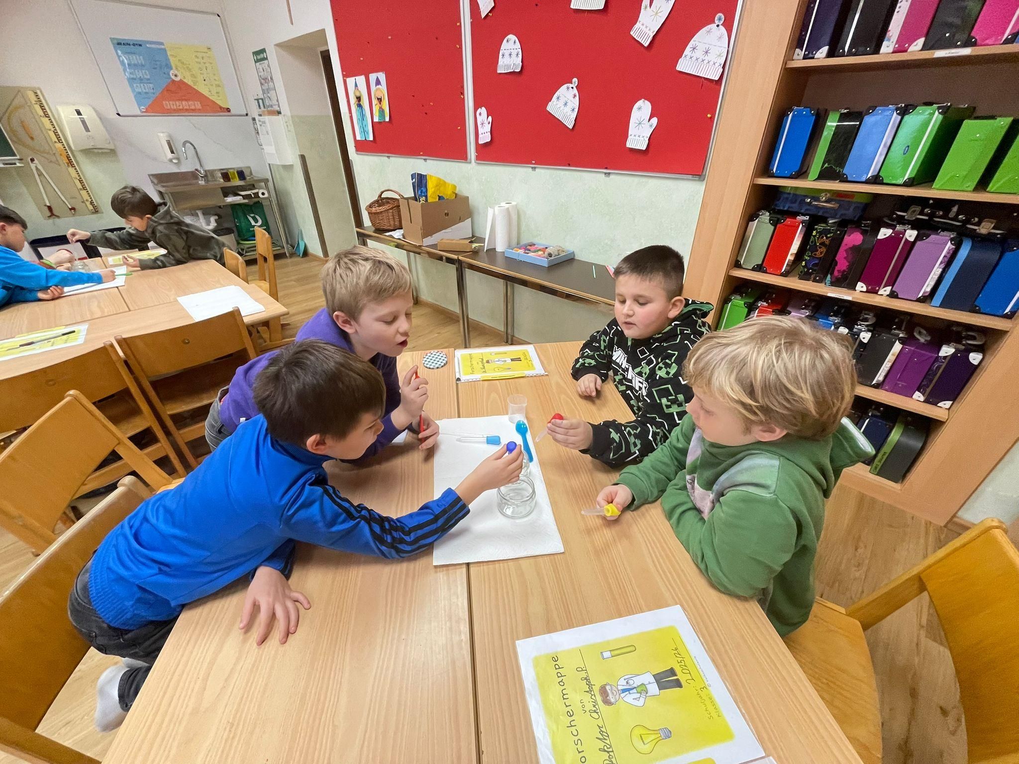 Vier Jungen sind in einem Klassenzimmer an einem Tisch mit einem wissenschaftlichen Experiment beschäftigt. Ein Junge benutzt eine Pipette, um Flüssigkeit in ein Glas zu übertragen.