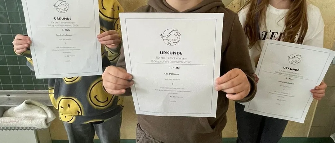 Drei Kinder stehen zusammen und halten Urkunden in der Hand, ein Junge in einer braunen Kapuzenjacke, ein anderer in einem gelben Shirt und ein Mädchen in einem weißen Shirt. Sie lächeln und posieren für ein Foto.