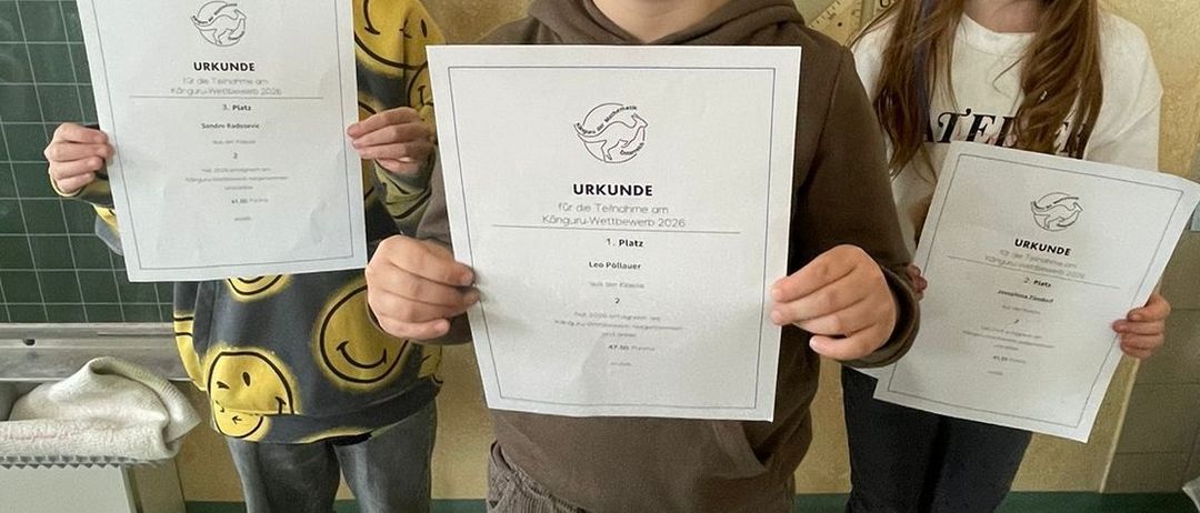 Drei Kinder stehen zusammen und halten Urkunden in der Hand, ein Junge in einer braunen Kapuzenjacke, ein anderer in einem gelben Shirt und ein Mädchen in einem weißen Shirt. Sie lächeln und posieren für ein Foto.