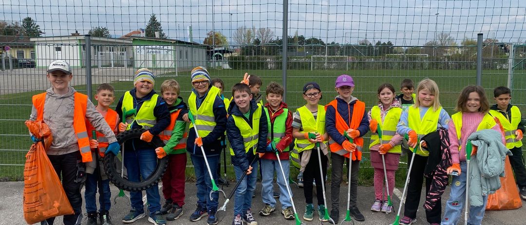 Eine Gruppe von Kindern in Sicherheitswesten und Handschuhen steht in einer Reihe, hält Werkzeuge und posiert für ein Foto.