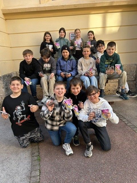 Eine Gruppe von Kindern, die auf einer Bank sitzen, kleine Pakete halten und für ein Foto posieren.
