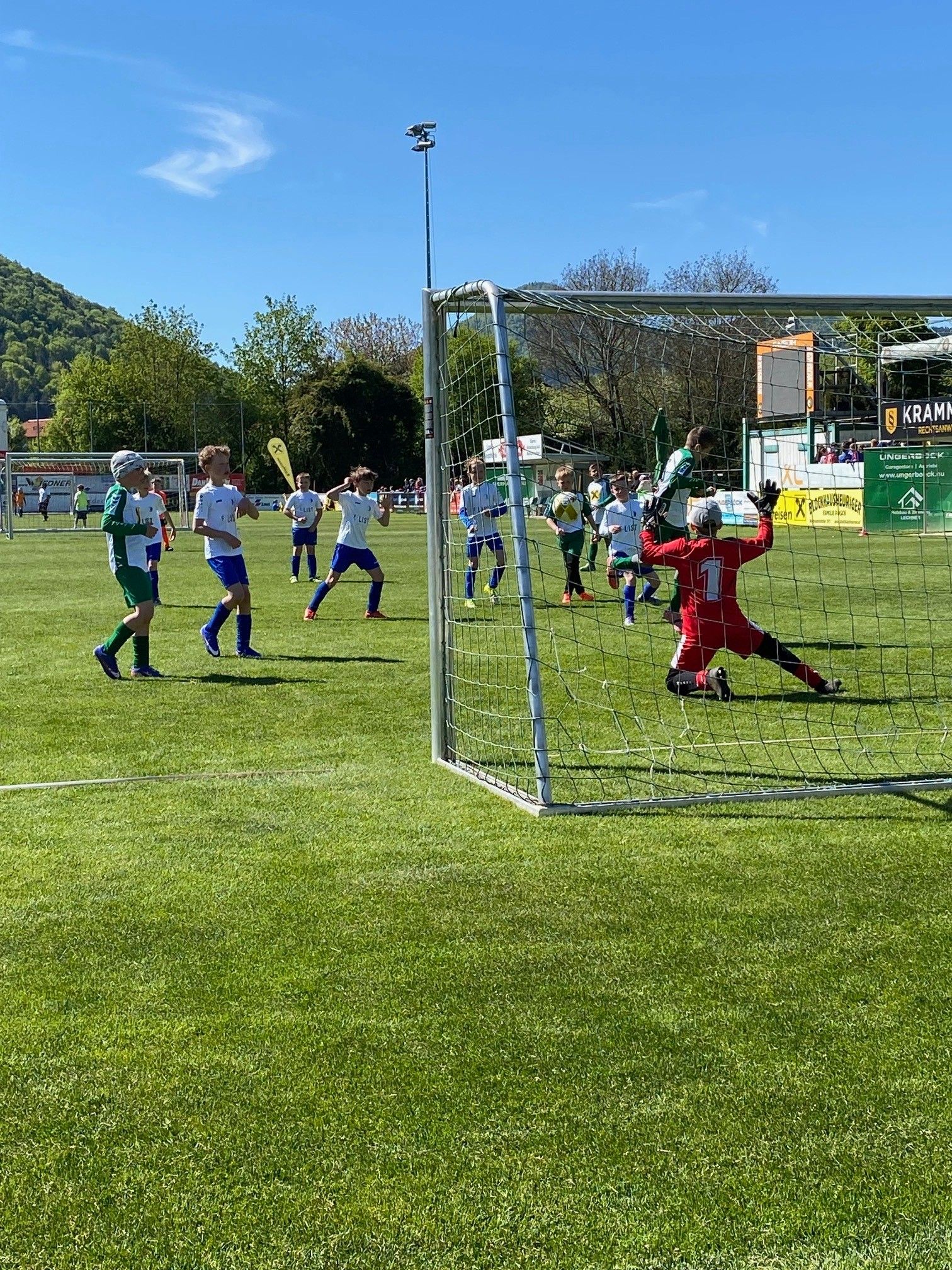 Eine Gruppe junger Fußballspieler auf einem Feld, wobei ein Spieler versucht, ein Tor zu blockieren.