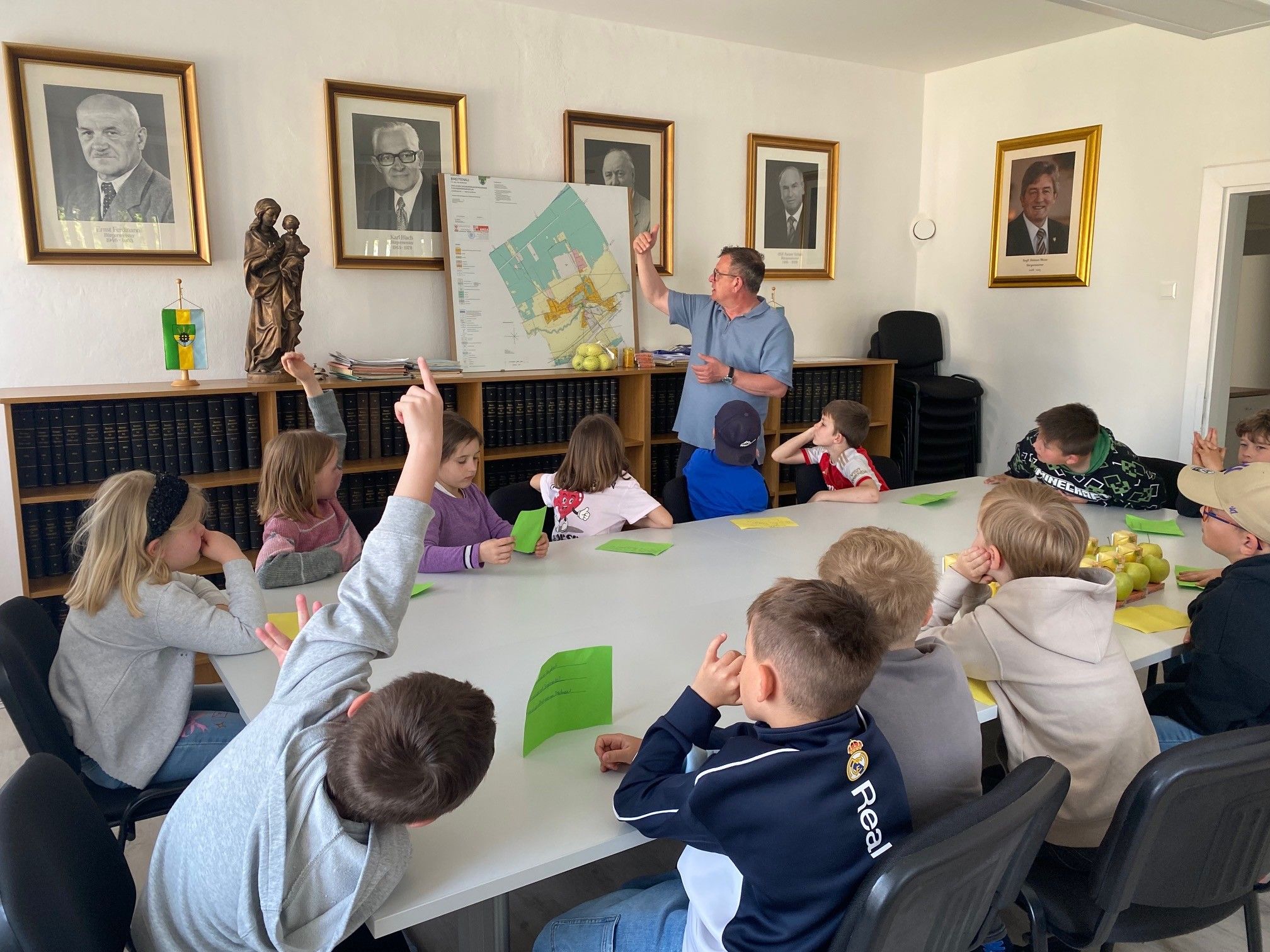 Ein Klassenzimmer mit einem Lehrer, der auf eine Karte an der Wand zeigt, während die Kinder aufmerksam zuhören.