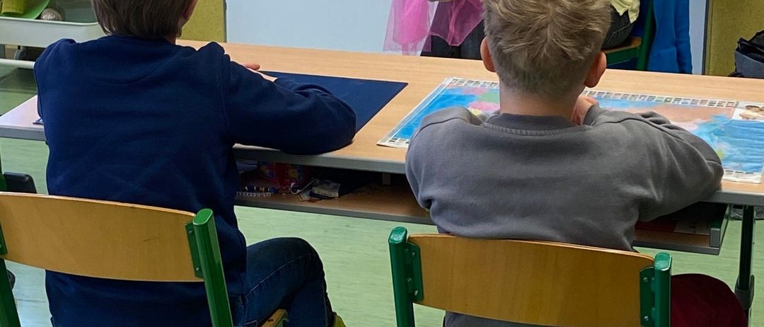 Eine Lehrerin benutzt eine Puppe, um junge Schüler in einem Klassenzimmer zu beschäftigen. Die Kinder sitzen an einem Tisch und lauschen aufmerksam.