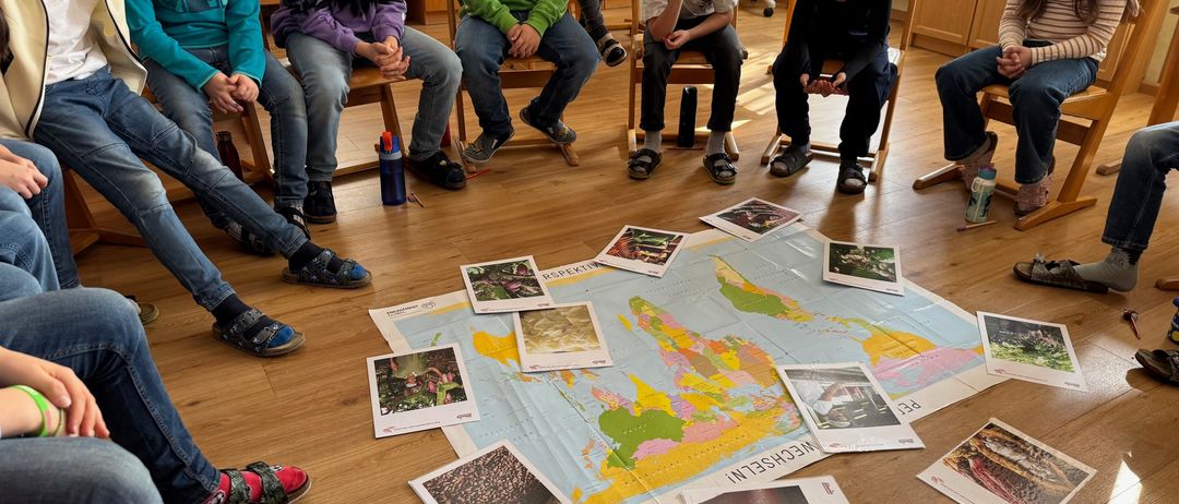 Eine Gruppe von Kindern sitzt um eine große Weltkarte auf dem Boden und studiert verschiedene Bilder und Karten.