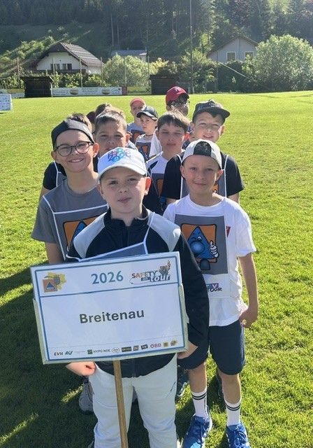 Eine Gruppe junger Jungen in Sportuniformen steht auf einem Rasenfeld, einer hält ein Schild mit der Aufschrift Breitenau.