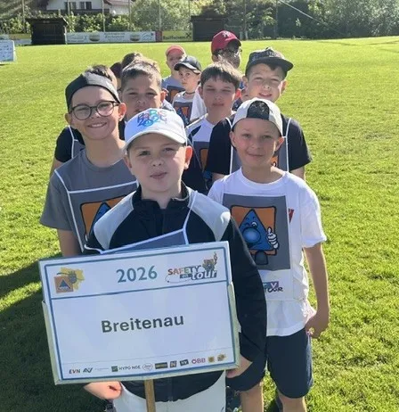 Eine Gruppe junger Jungen in Sportuniformen steht auf einem Rasenfeld, einer hält ein Schild mit der Aufschrift Breitenau 2026.