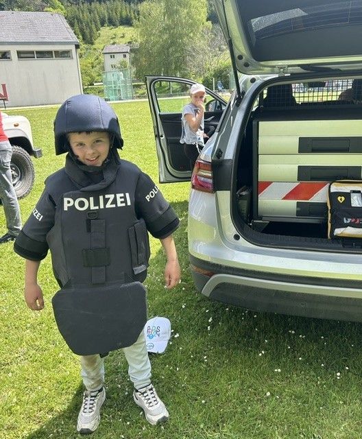Ein junger Junge in einer Polizeiuniform steht auf einem Rasen, mit einem Polizeiauto im Hintergrund.
