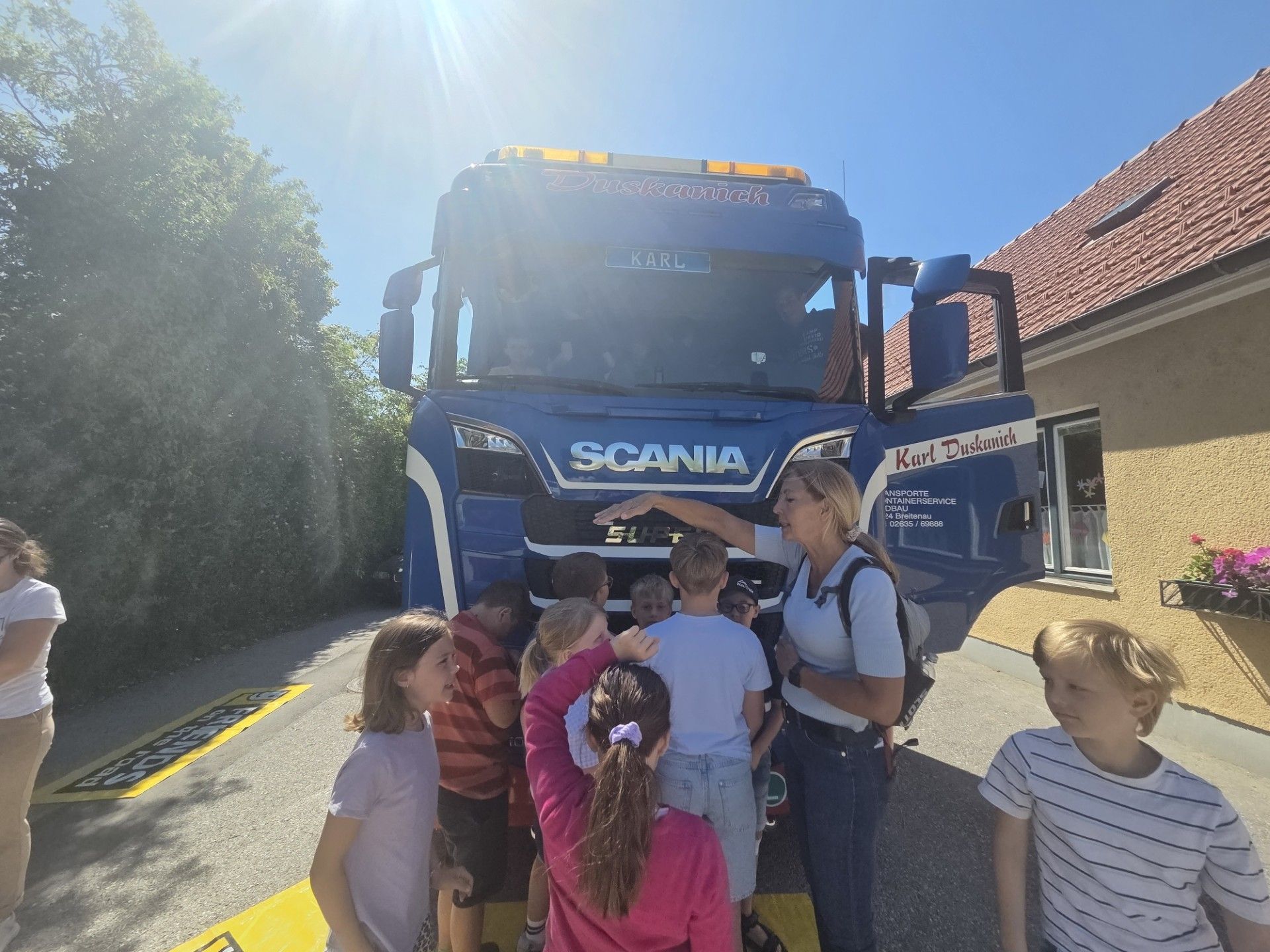 Eine Frau mit Rucksack erklärt etwas einer Gruppe von Kindern vor einem Scania-Lkw.