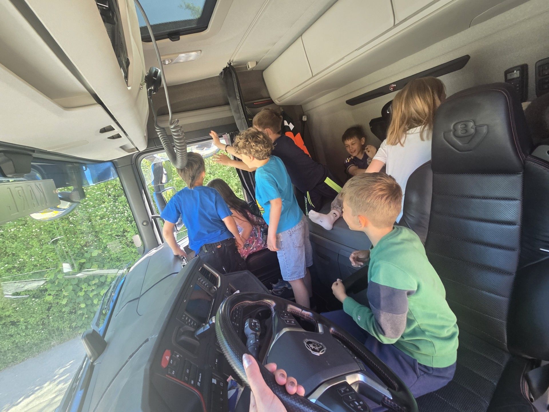 Eine Gruppe von Kindern sitzt in einem Bus, einige schauen aus dem Fenster, und eine Person hält das Lenkrad.