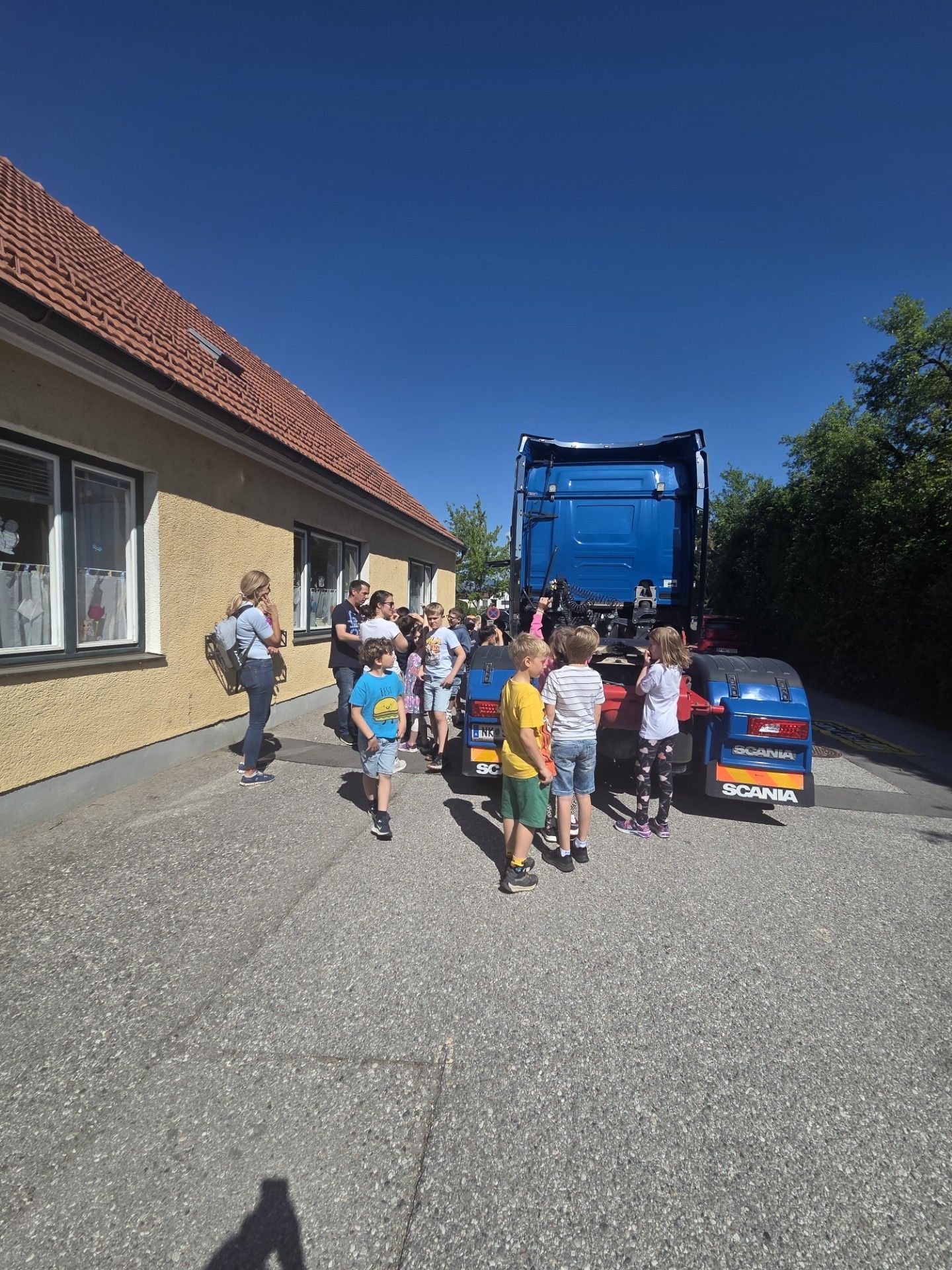 Eine Gruppe von Kindern und Erwachsenen versammelt sich um einen blauen Scania-Lkw auf einem Parkplatz.