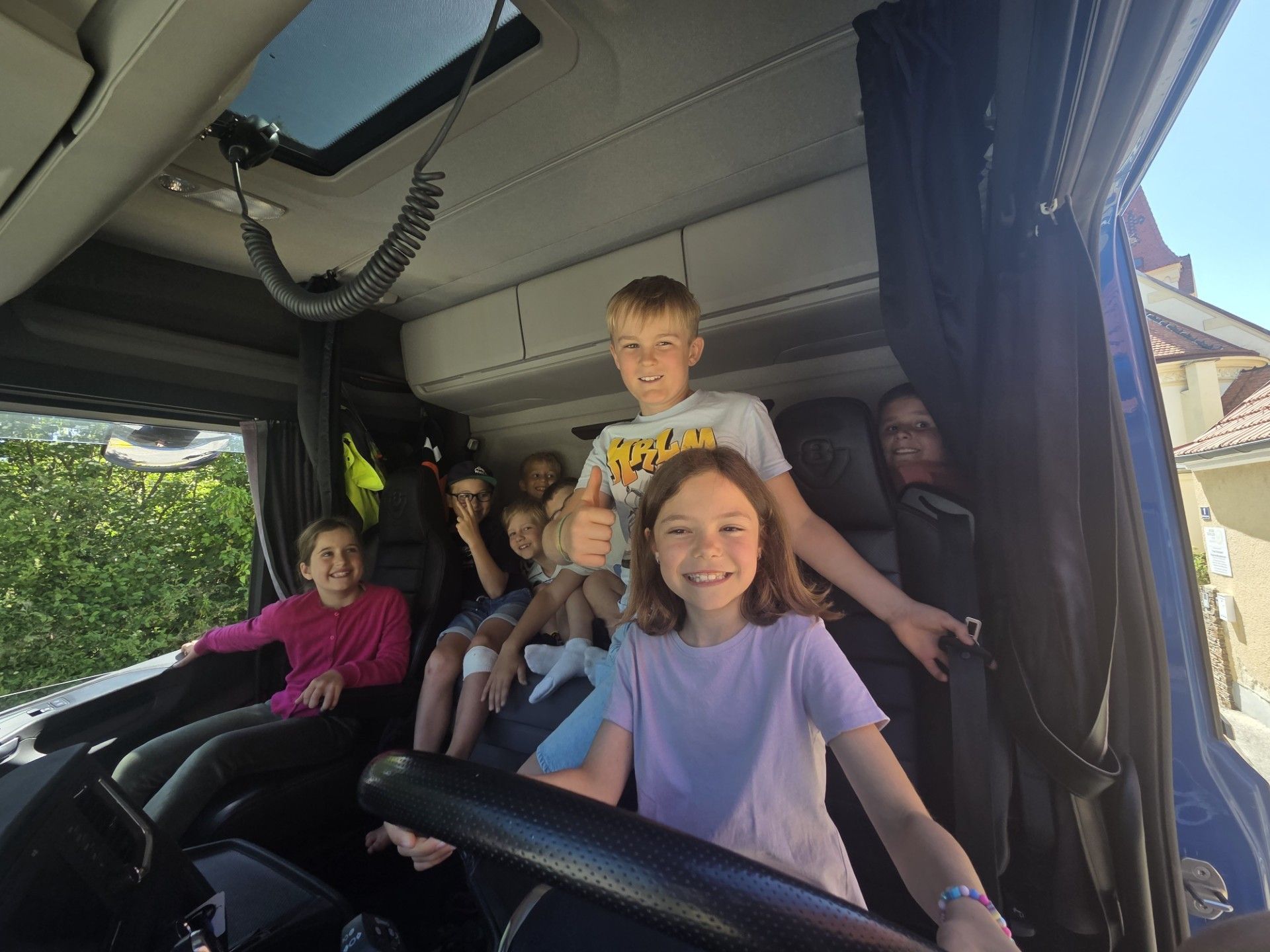 Eine Gruppe von Kindern und einer Frau sind in einem Fahrzeug und posieren für ein Foto. Der Junge in der Mitte gibt einen Daumen hoch.