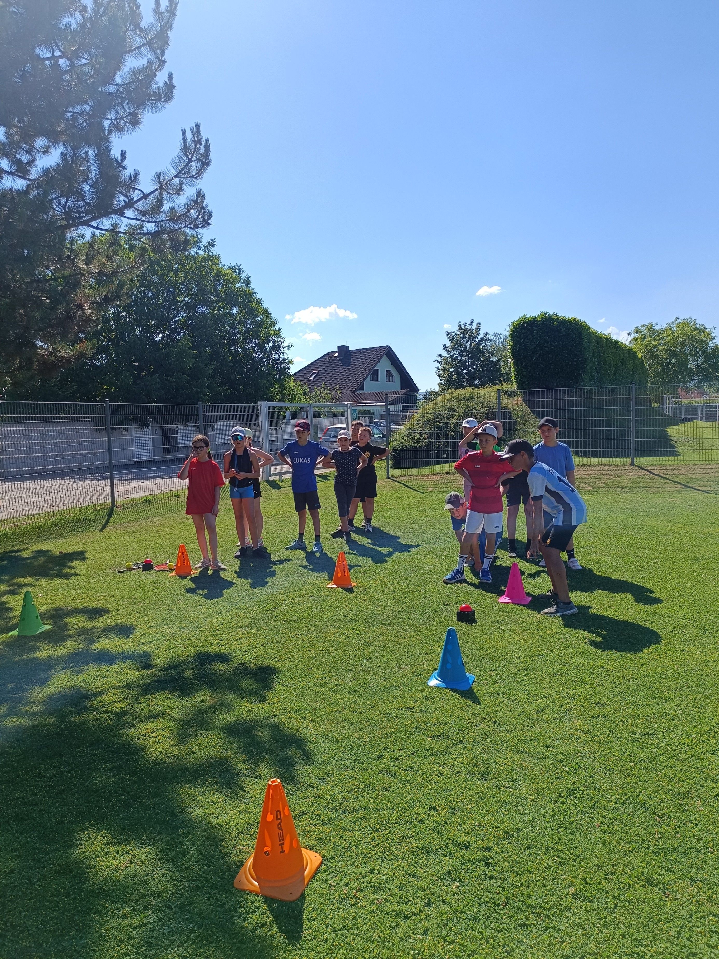 Eine Gruppe von Kindern auf einem Spielplatz, die Mützen und Turnschuhe tragen, nehmen an einem Spiel mit Kegeln und Bällen teil.