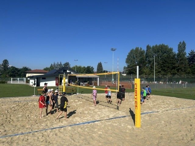 Eine Gruppe von Menschen spielt Volleyball auf einem sandigen Platz mit einem Netz in der Mitte.