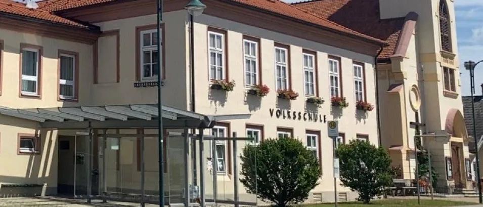 Ein Luftbild eines Gebäudes mit mehreren Fenstern und einem braunen Dach. Das Gebäude befindet sich an einer Straße mit einem Gehweg und einem Rasenbereich.