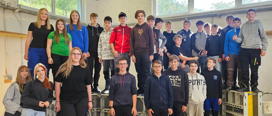 Eine Gruppe junger Menschen steht auf Kisten in einem Raum und lächelt für ein Foto.